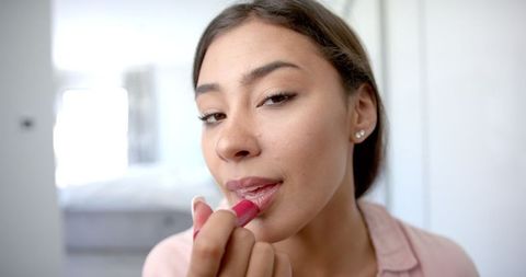 Smiling Woman Applies Lipstick in Cozy Home Environment