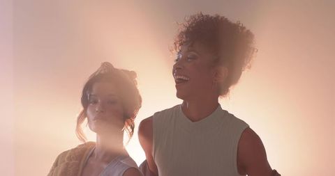 Two diverse women radiating warm backlit glow while laughing and embracing minimalist fashion