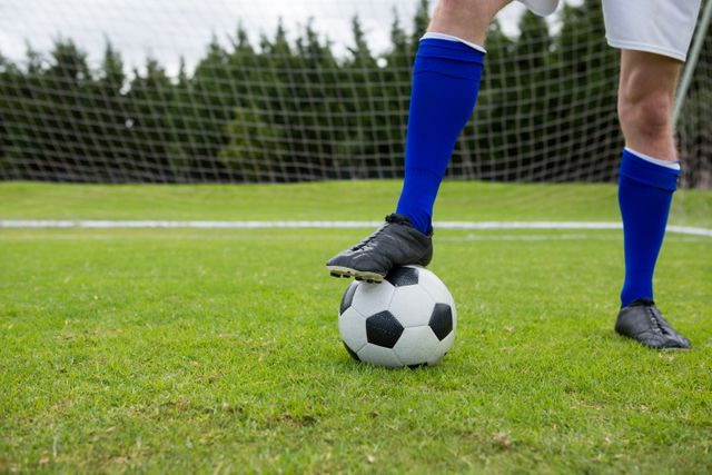 Low section of male soccer player with ball on field against goal post