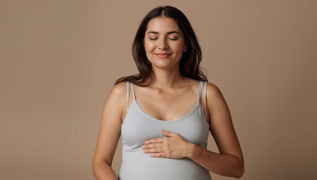 Pregnant woman smiling with eyes closed, resting hand on belly, wearing light gray tank top