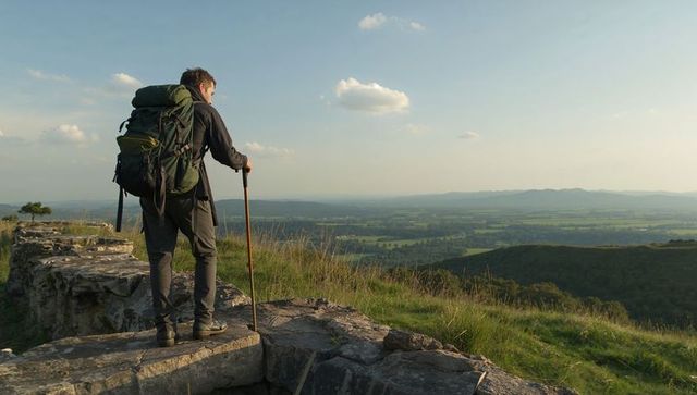 Hiker standing on rock ledge overlooking panoramic valley landscape at golden hour