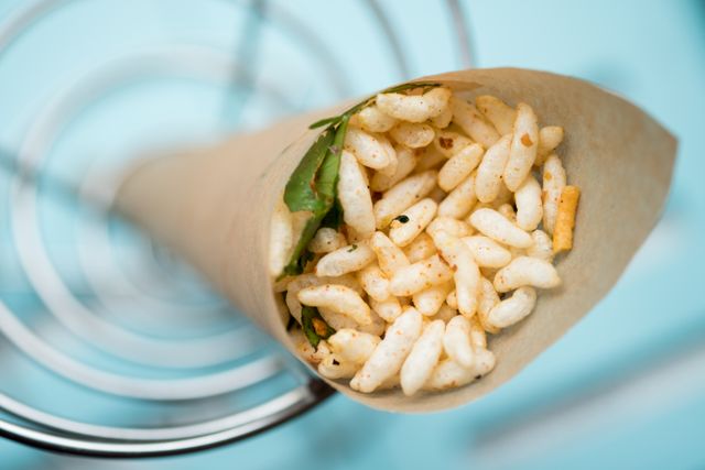 Puffed rice snack, commonly known as murmura, served in a paper cone. The mixture is seasoned and garnished with herbs. Ideal for use in blogs about Indian cuisine, food photography, or magazine articles highlighting traditional snacks and street food.