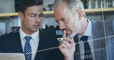 Two business partners analyzing strategy on laptop while leaning at cafe counter for teams