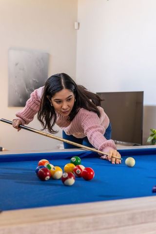 Asian woman aiming cue on blue-felt pool table at home while concentrating on shot