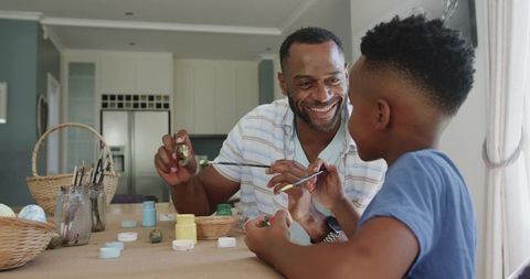 African american father and son painting together at kitchen table, bonding through art