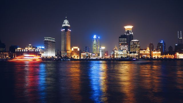 A vibrant nighttime view of Shanghai's skyline with the Huangpu River in the foreground. The illuminated skyscrapers reflecting on the water create a captivating and dynamic urban scene. Perfect for projects related to travel, tourism, city life, and modern architecture.