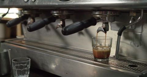 Espresso pouring into short glass on stainless commercial espresso machine with crema