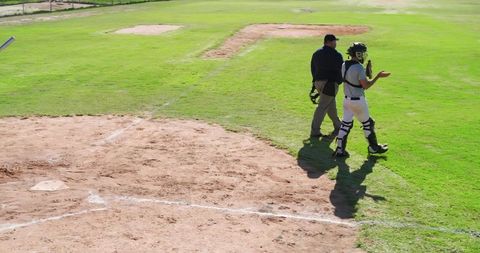 Catcher and umpire walking near home plate on sunny baseball field