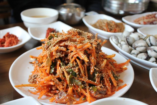Delicious Korean carrot salad garnished with sesame seeds served on a table with various side dishes. Perfect for articles on traditional Korean cuisine, healthy eating, or Asian recipes.