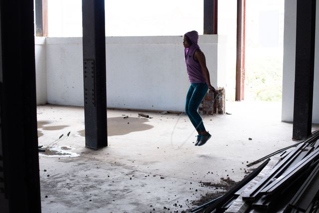 African american woman wearing sports clothes skipping the rope in empty urban building. urban fitness healthy lifetyle.