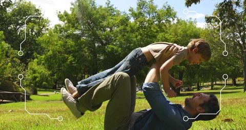 Father lifting son while playing on sunny park lawn, joyful fatherhood and family bonding