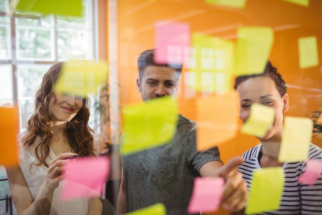 Business professionals engaged in brainstorming session using colorful sticky notes. Ideal for illustrating concepts of teamwork, creative thinking, planning, and strategy development in modern workplaces.