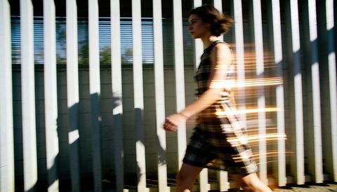 Woman walking past vertical slats with motion blur and golden light streaks