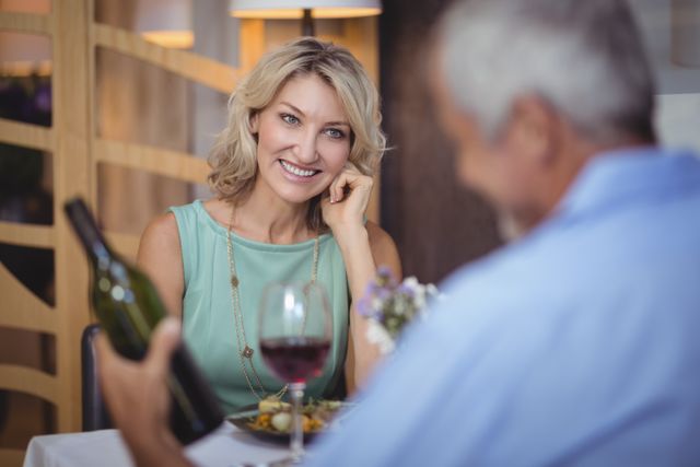Mature couple enjoying a romantic dinner with red wine at a restaurant. The woman is smiling warmly at her partner. Ideal for use in advertisements for restaurants, romantic getaways, lifestyle blogs, and articles about relationships and dining experiences.