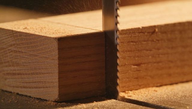 Cutting hardwood plank with vertical band saw blade throwing sawdust close-up macro