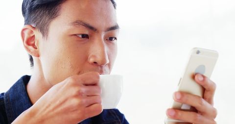 Man Drinking Coffee While Browsing Smartphone