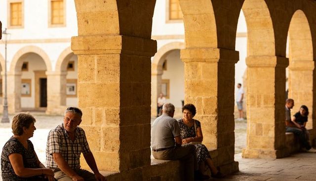 Seniors conversing under sunlit sandstone arches in historic mediterranean colonnade