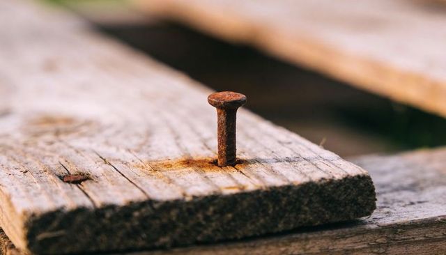 Rusty nail protruding from weathered wood macro texture with rust stain detail