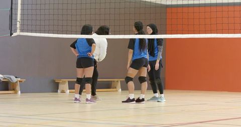 Multicultural women's volleyball team huddling at net with coach giving tactical instruction