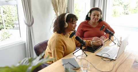 Multiracial women cohosting home podcast, recording and collaborating with laptop