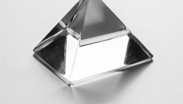 Minimal crystal pyramid reflecting studio light on gray surface with sharp facets and mirror shine