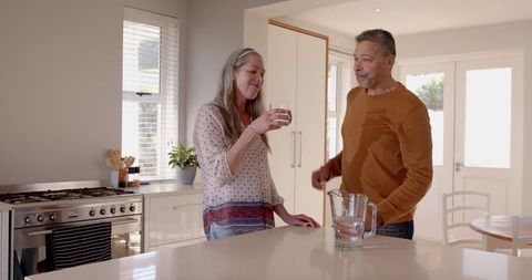 Senior Couple Sharing Toast with Water in Bright Kitchen