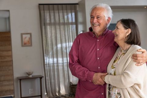 Senior couple embracing in cozy modern home with sheer curtain background