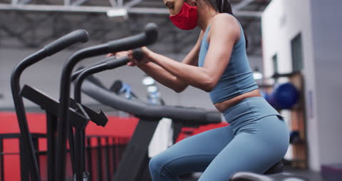 Mask-Wearing Woman Exercising on Cross Trainer in Gym