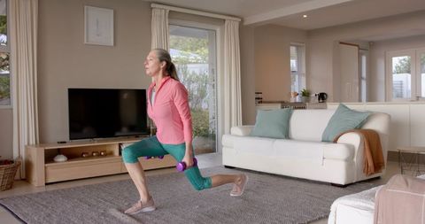 Senior woman exercising with dumbbells in living room for fitness