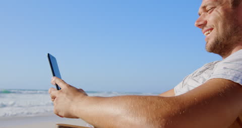 Young Man Relaxing at Beach Using Smartphone on Sunny Day