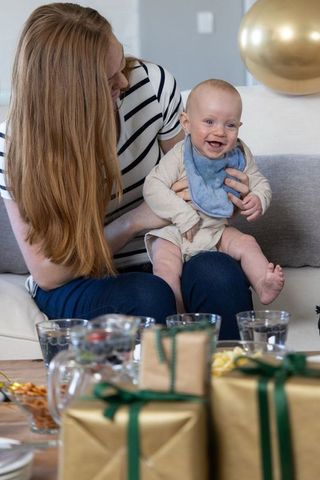 Smiling Baby on Couch with Mother Near Wrapped Gifts at Family Gathering