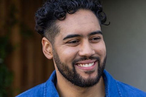 Smiling bearded man wearing blue denim jacket looking right outdoor headshot natural daylight