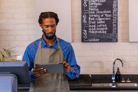 African american barista using tablet at modern coffee counter with chalkboard menu