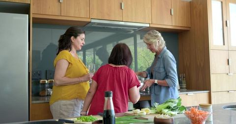 Diverse women preparing meal at kitchen island chopping vegetables and stirring pot