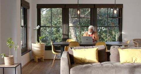 Senior man working on laptop in modern home office with natural light