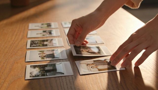 Hands arranging instant polaroid prints on wooden table in warm sunlight, nostalgic mood