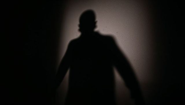 Backlit shadow of man in coat on textured wall, dramatic silhouette with chiaroscuro light