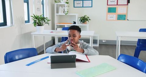 African American boy using tablet and studying with headphones in modern classroom focus
