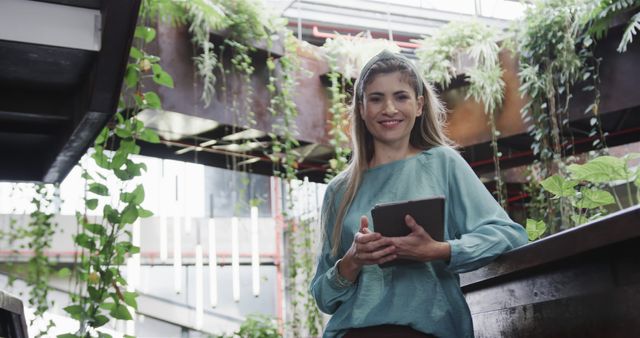 Smiling businesswoman holding tablet in modern office with plants design - Download Free Stock Images Pikwizard.com