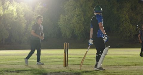 Night cricket match featuring batsman in helmet and pads at crease under floodlights
