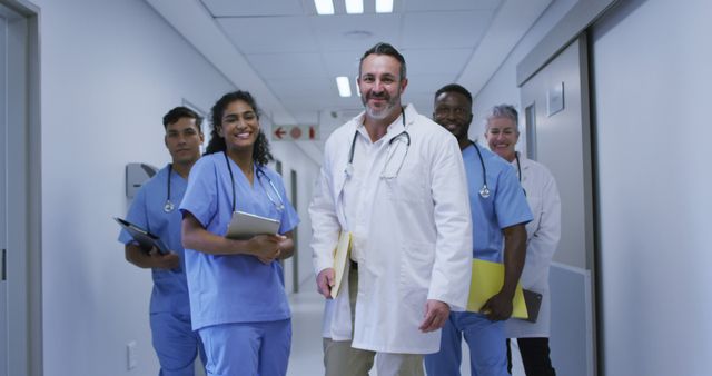 Diverse group of smiling male and female doctors in hospital corridor wearing scrubs and lab coats. medicine, health and healthcare services.