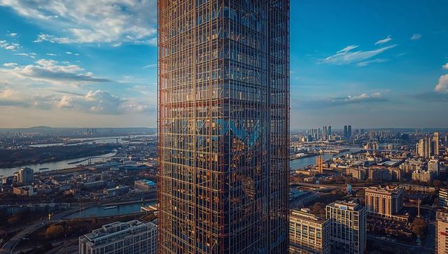 Glass skyscraper reflecting riverside cityscape with bridges at golden hour, aerial view