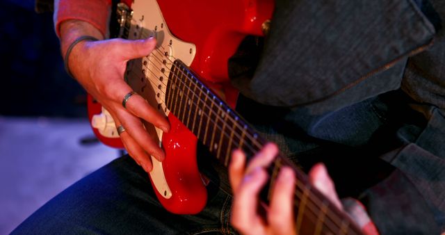 Image of a guitarist playing a red electric guitar, focusing on the hands and the instrument. Great for use in articles about music performance, musician profiles, rock bands, music education, or guitar tutorials.