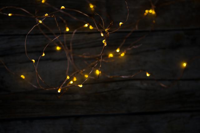 Warm yellow fairy lights glowing against a rustic wooden background. Ideal for use in holiday-themed designs, festive invitations, cozy home decor inspiration, and creating a warm, inviting atmosphere in digital or print media.