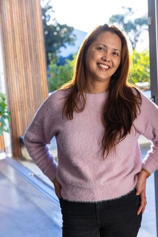 Relaxed asian woman smiling by patio door in cozy pink sweater
