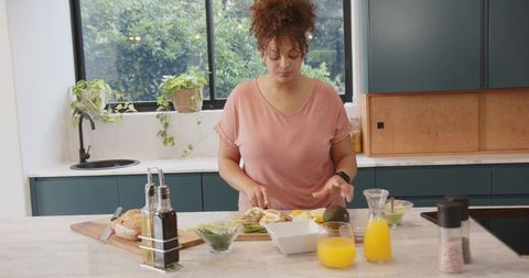 African american woman preparing avocado toast and fresh juice in modern sunlit kitchen