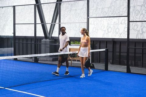 Diverse duo walking on blue padel court with rackets