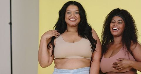 Plus-size diverse women laughing and posing in sports bras on bright yellow backdrop