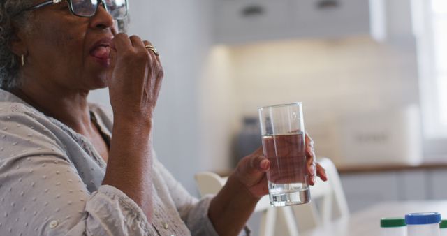 Senior woman taking medication with a glass of water at home. Great for topics on healthcare, senior care, daily routines for the elderly, and health lifestyle tips for older adults.