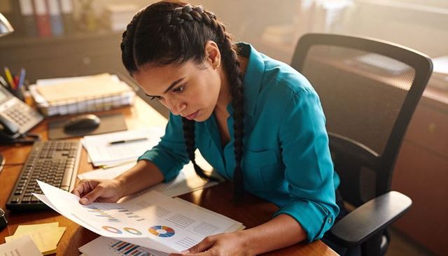 Businesswoman analyzing financial reports at desk with charts and keyboard